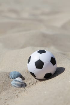 A soccer ball lying in the sand on the beach.