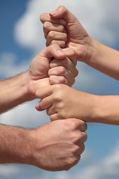 Some people putting her hands together in front of a bright blue sky.