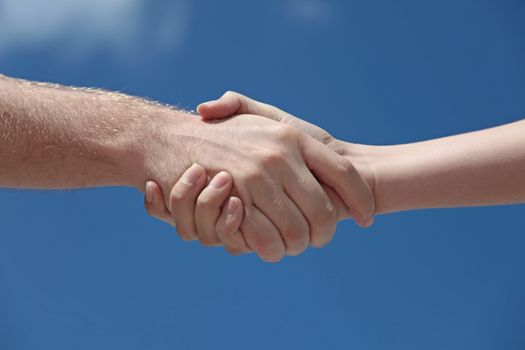 A man and woman handshaking in front of a bright blue sky.