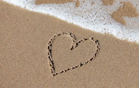 Heart on sand beach being washed away.