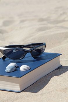 A book and sunglasses lying in the sand, symbolizing recreation.