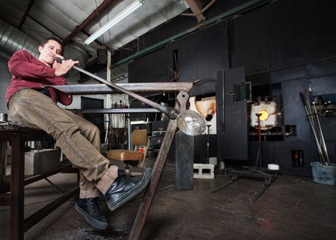 Wide angle view of artisan blowing into fine art glass