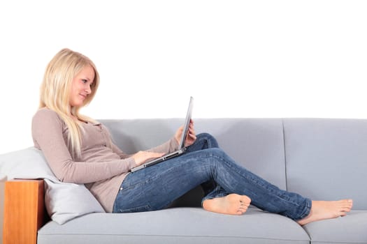 An attractive young woman using her notebook computer while sitting on a couch.