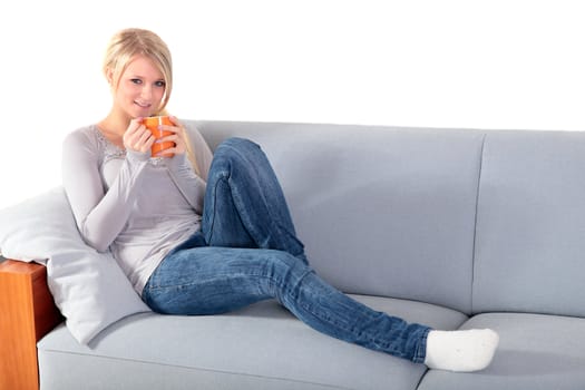An attractive young woman enjoys a cup of coffee while sitting on a couch.