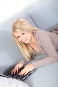 An attractive young woman using her notebook computer while sitting on a couch.