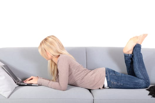 An attractive young woman using her notebook computer while lying on a couch.