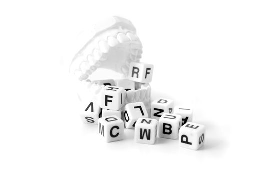 A plaster cast of teeth with a lot of dices showing different letters. All on white background.