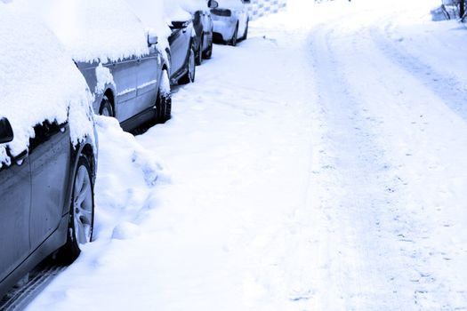 Several cars parking on a snowbound street.