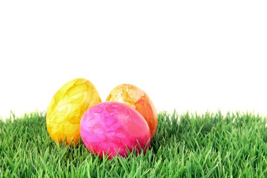 Three multicolored easter eggs lying on a fine green meadow. All on white background.