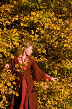 The blonde girl in medieval red dress in the autumn forest
