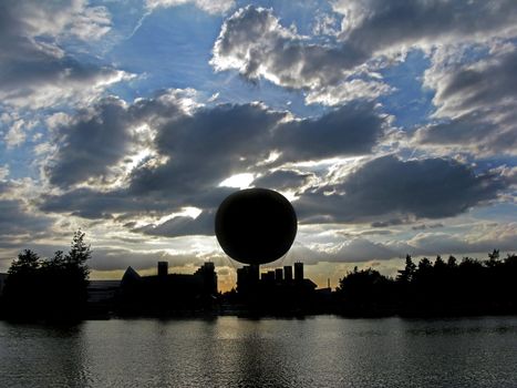 A silhouette of a balloon and surroundings at sunset across a lake.