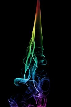 A rainbow colored smoke trail from an incense stick. Black background.