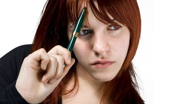 Cute girl with red hair holding a pen against her forehead and thinking.

Studio shot.