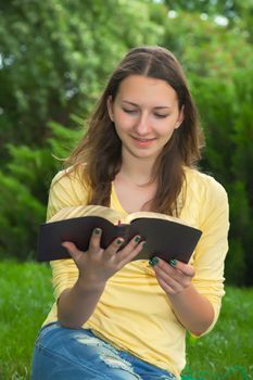 Teen girl reading book outdoors at summer time