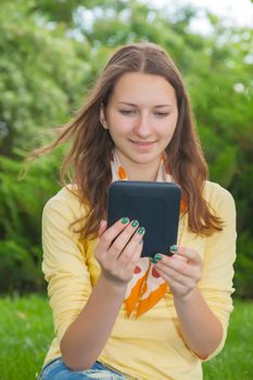 Teen girl reading electronic book outdoors