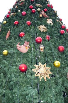 Synthetic Christmas tree decorated with lots of toys. Downtown scenery.