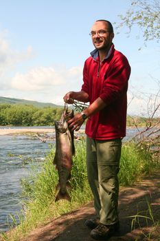 The fisherman with the fish on the river bank, Kamchatka