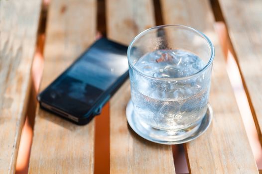 water drink and ice in glass with mobilephone on wood table