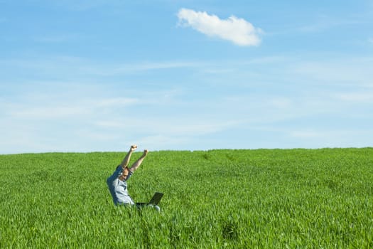 young man uses a laptop in the green field