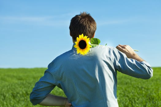 young man standing with a sunflower in the green field