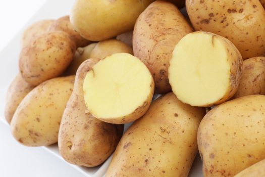 Closeup of a farmers market display of fresh whole potatoes with one cut through in half to show the firm flesh