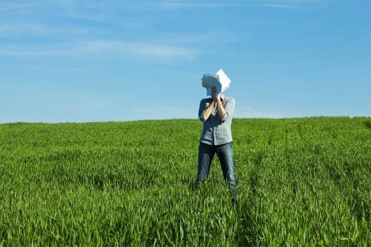 young man covering the face paper in green field