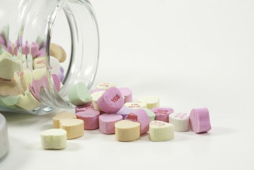 a jar of valentine hearts spilled on white background