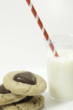 stack of three cookies with chocolate hearts and glass of milk with a striped red straw view from above with white background