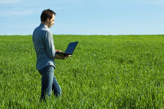 young man uses a laptop in the green field