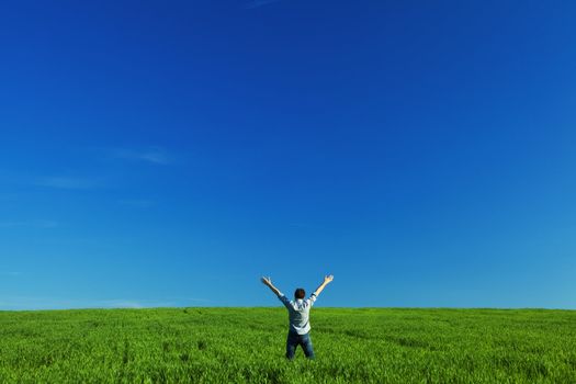 young man outstretched arms in green field against the blue sky