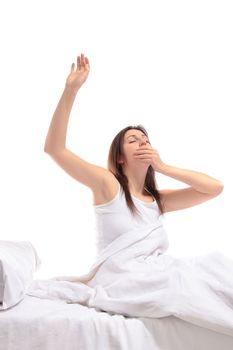 A young woman yawning while sitting on her bed. All on white background.