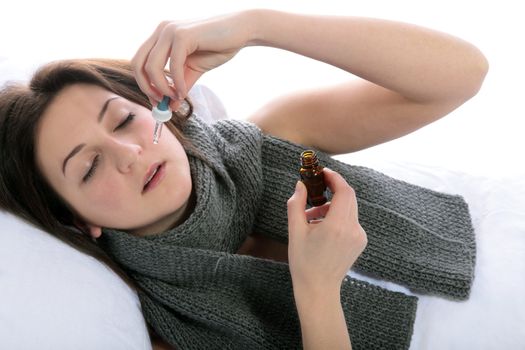 A young woman lying in bed using nosedrops. All on white background.