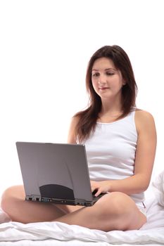 A young woman sitting on her bed using a notebook computer. All on white background.