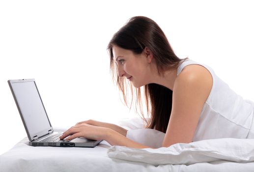 A young woman lying in her bed using a notebook computer. All on white background.