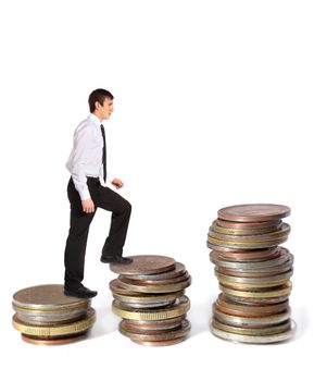 A young businessman walking up several pile of coins. All on white background.