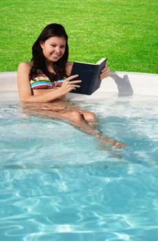 An attractive young girl reading a book in the swimming pool.