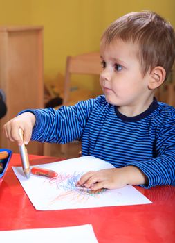 Cute caucasian toddler drawing a picture in kindergarten.