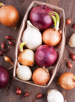 Different varieties of onions on a kitchen board and wooden surface