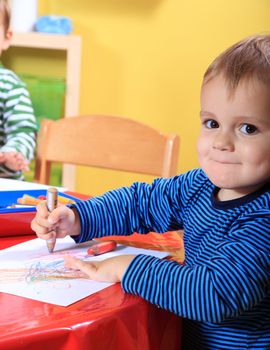 Cute caucasian toddler drawing a picture in kindergarten.