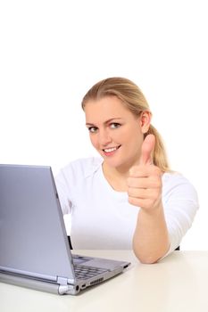 Attractive blonde woman making thumbs up sign while working at her notebook computer. All on white background.