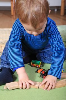 Cute european toddler playing with toy train in kindergarten.