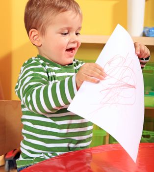 Cute caucasian toddler shows his drawn picture in kindergarten.