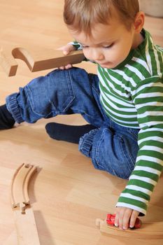 Cute european toddler playing with toy train in kindergarten.