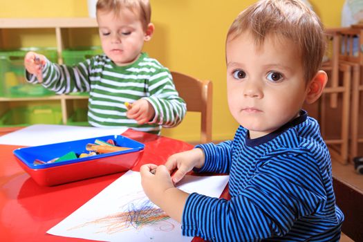 Cute european toddlers drawing a picture in kindergarten.