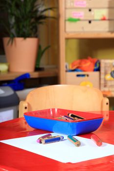 Desk in kindergarten with paper and colored pencils.