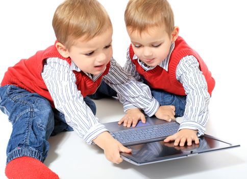 Cute caucasian twin brothers playing with notebook computer. All isolated on white background. Foreground in very light grey.