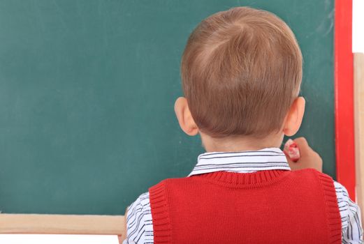 Cute caucasian toddler doodling on chalkboard. All isolated on white background.