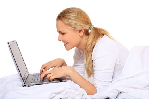 Attractive blond woman using notebook computer while lying in bed. All on white background.