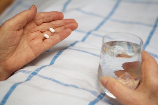 Care-dependent person taking her medicine in bed.