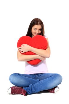 Attractive teenage girl holding heart-shaped red pillow. All on white background.